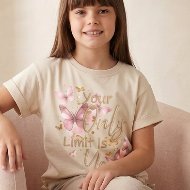 Young girl sitting on a pink chair wearing a white t-shirt with text and graphics.