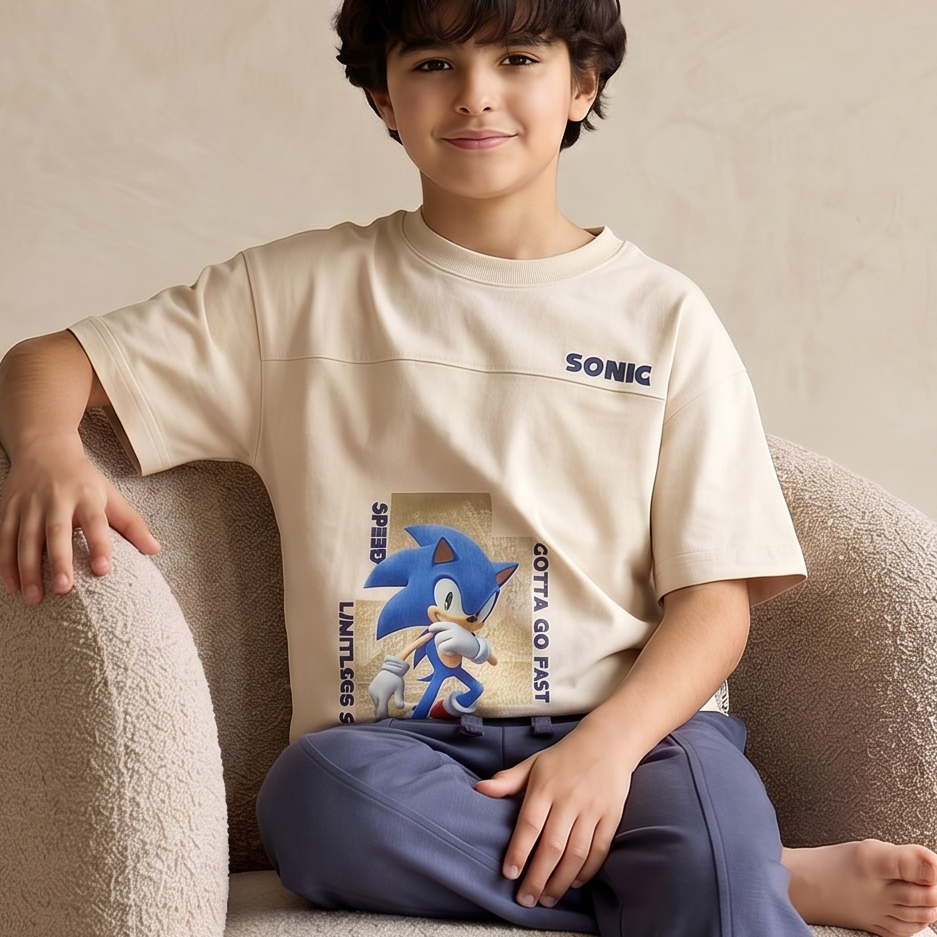 Child sitting on a beige armchair wearing a Sonic the Hedgehog t-shirt in a neutral-colored room.