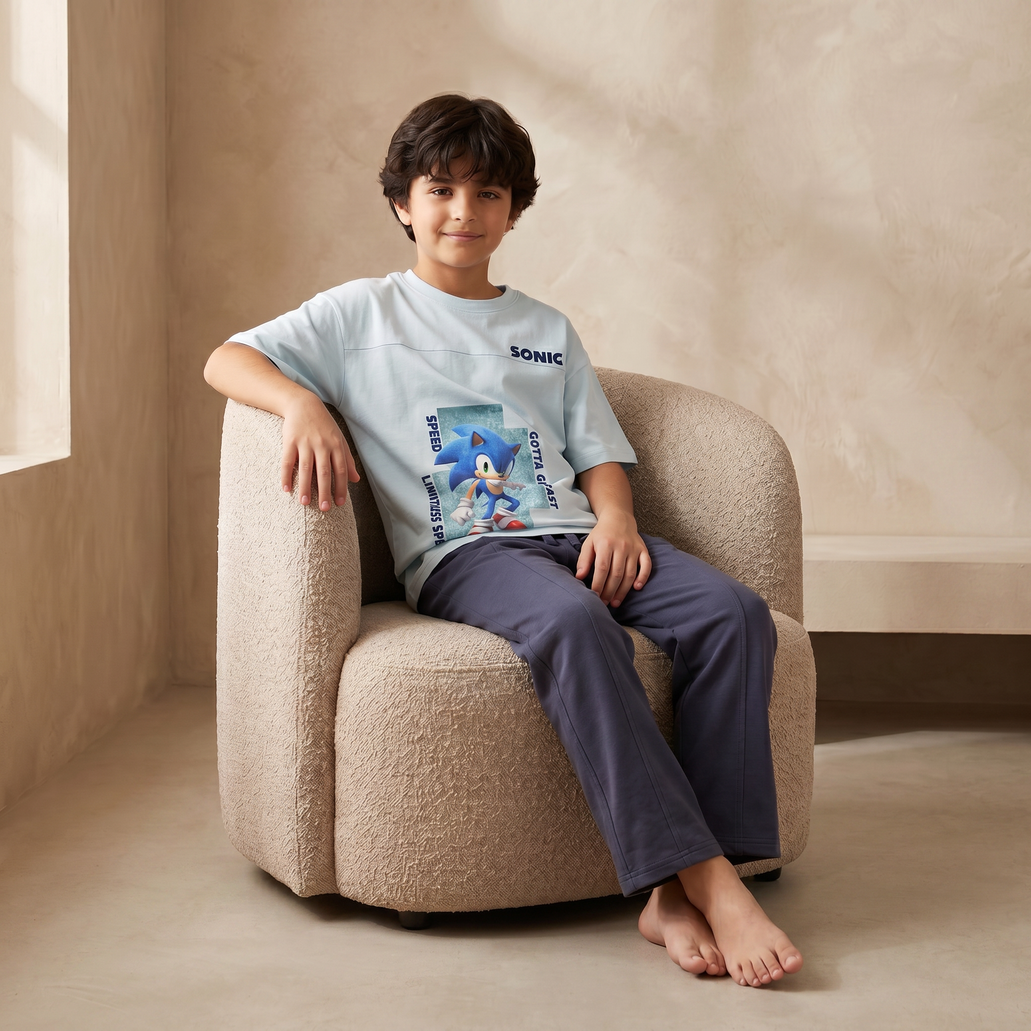 Child sitting on a beige armchair wearing a Sonic the Hedgehog t-shirt in a neutral-colored room.
